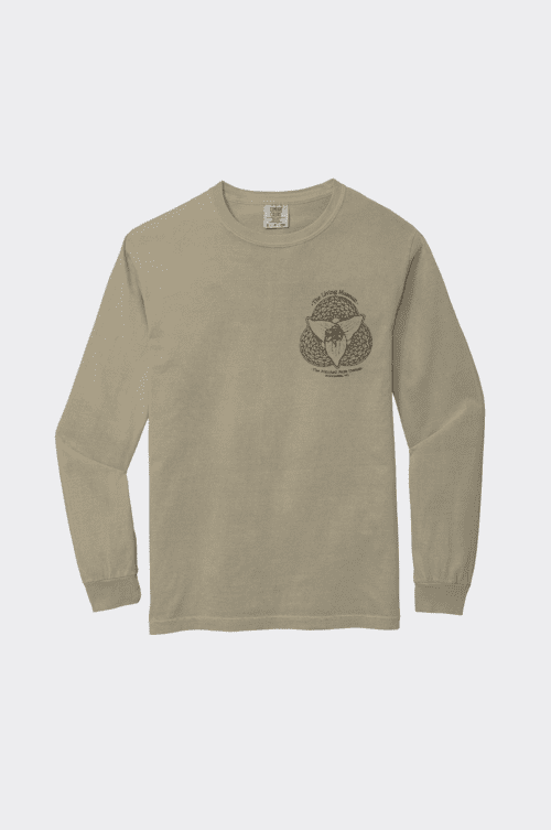 A khaki long sleeve T-shirt features a printed design with the text "The Living Museum" above an illustration of an insect combined with flowers. Below the design, it reads "The Mitchell Park Domes, Milwaukee, WI." The illustration is enclosed within a detailed geometric pattern.