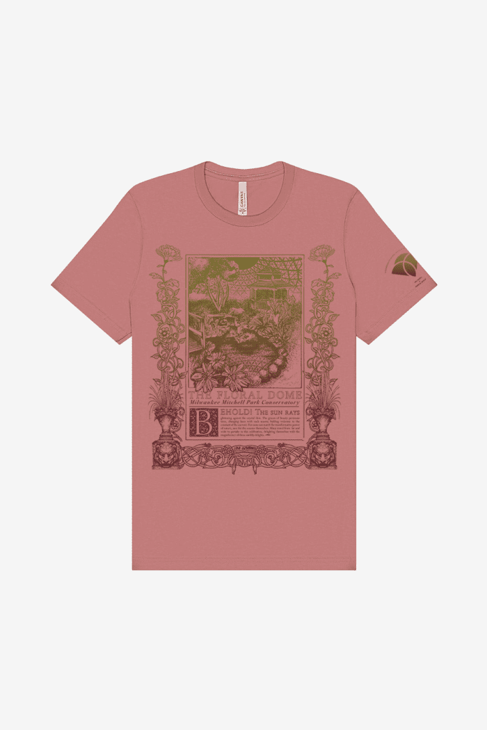 A mauve short-sleeve shirt with a vintage-style, art nouveau inspired illustration and text in olive green and coral. The design features various plants, a gazebo and pond, and ornate borders, with the words "The Tropical Dome" and "Milwaukee Mitchell Park Conservatory". Below is a poem, reading: "Behold! The sun rays glistening against the crystal dew. The graces of beauty permeate time, changing faces with each season; bidding welcome to the constant of the current. For none can match the transformative power of nature, save for the seasons themselves. Many travel from far and wide to partake in this celebration, delighting themselves with the magnificence of these earthly delights."
