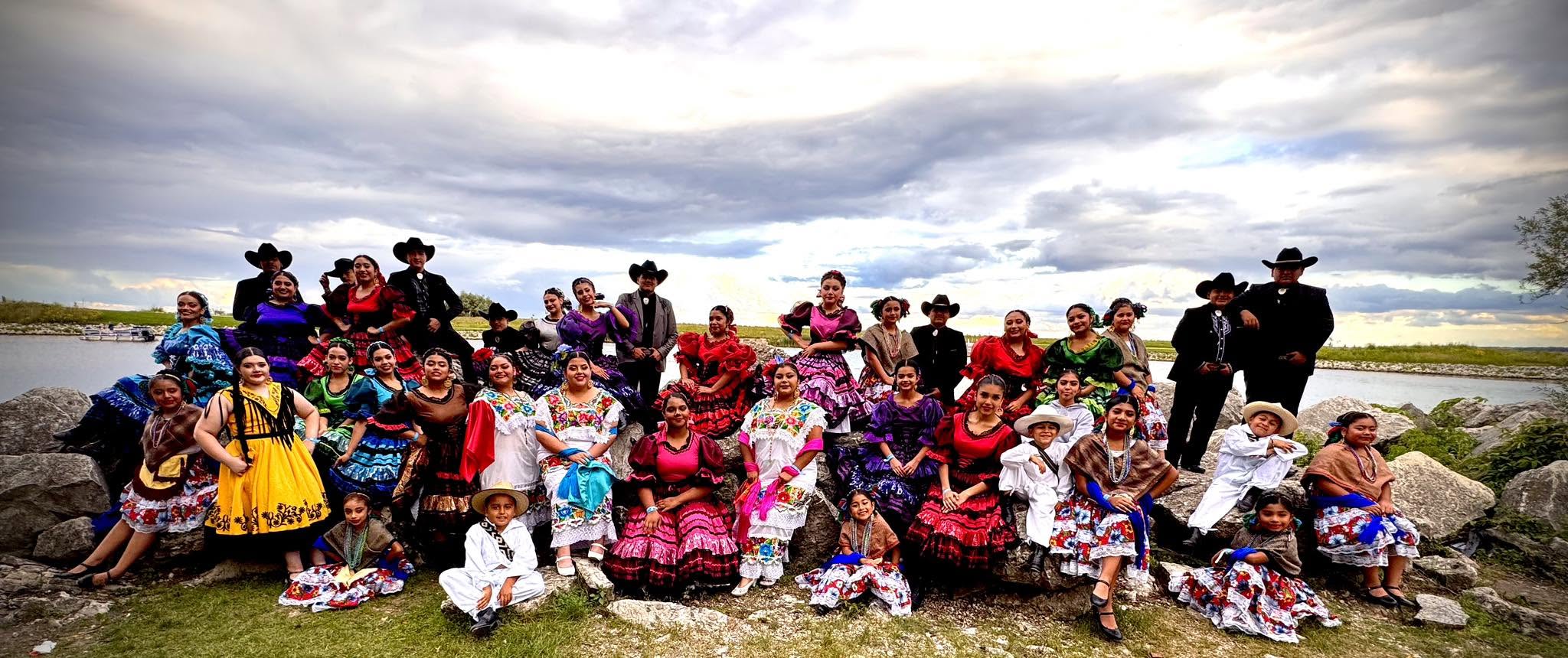 ICD Dance Company members in colorful costumes gathered outdoors beside the water.